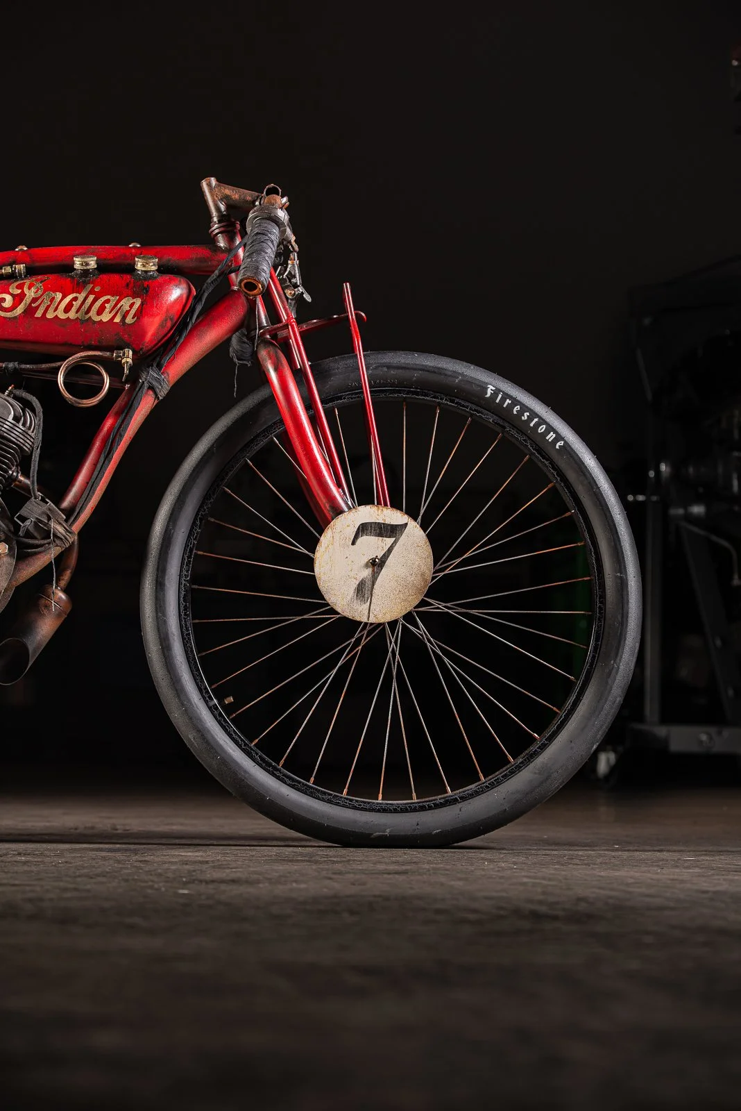 Close-up of vintage red Indian motorcycle front wheel with a rusty hub and black tire, set against a dark background.