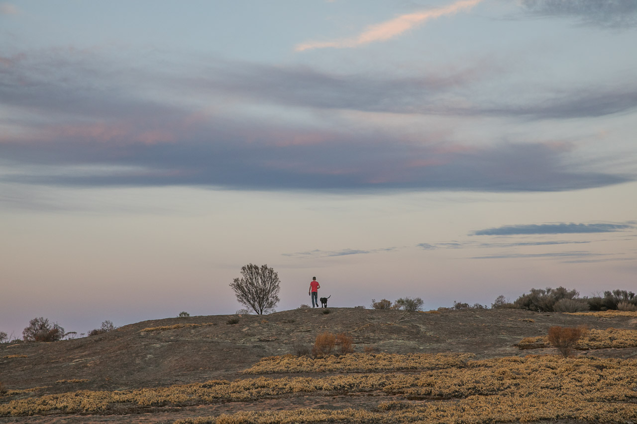 Man and dog walking on top of a granite outcrop in WA's wheatbelt at sunset