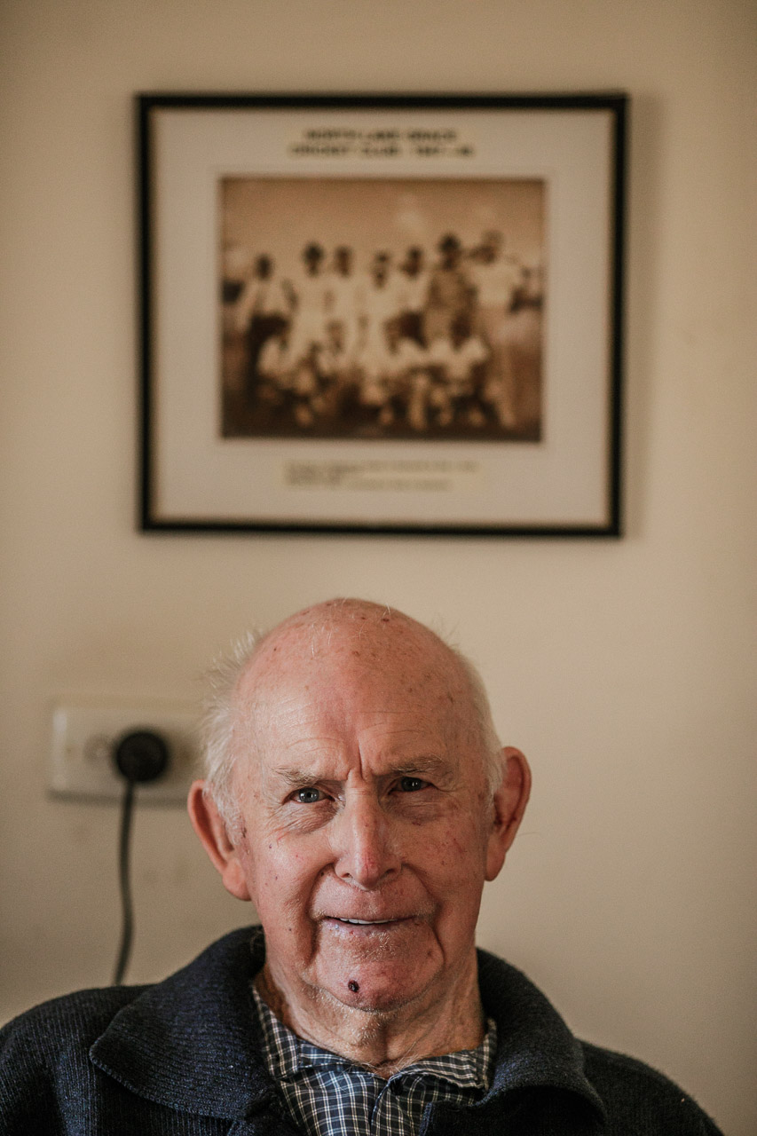 Elderly man smirking with an old framed photo of his cricket team