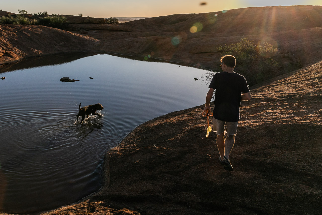 Rim lit man and dog at sunset with pool of water