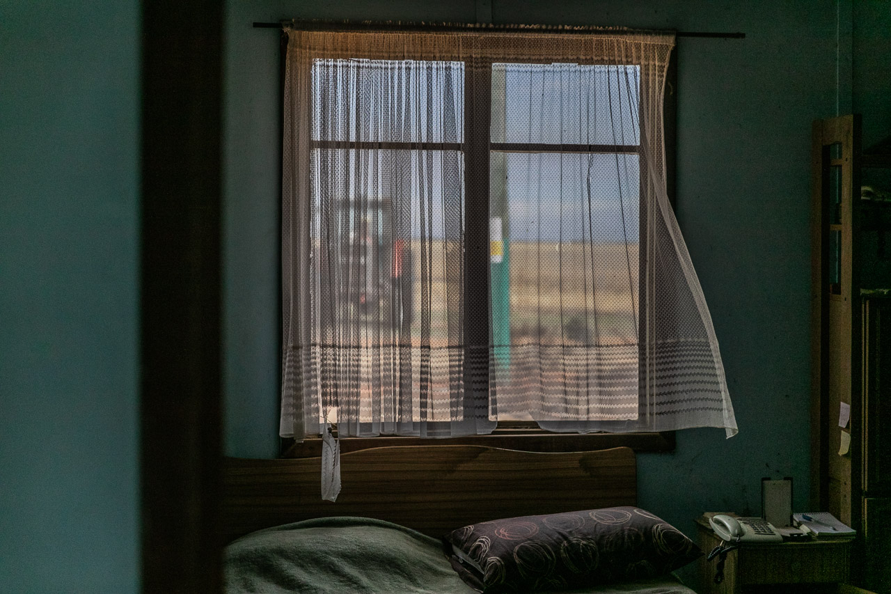 View through a shack window through torn net curtains to the tractor and wheat