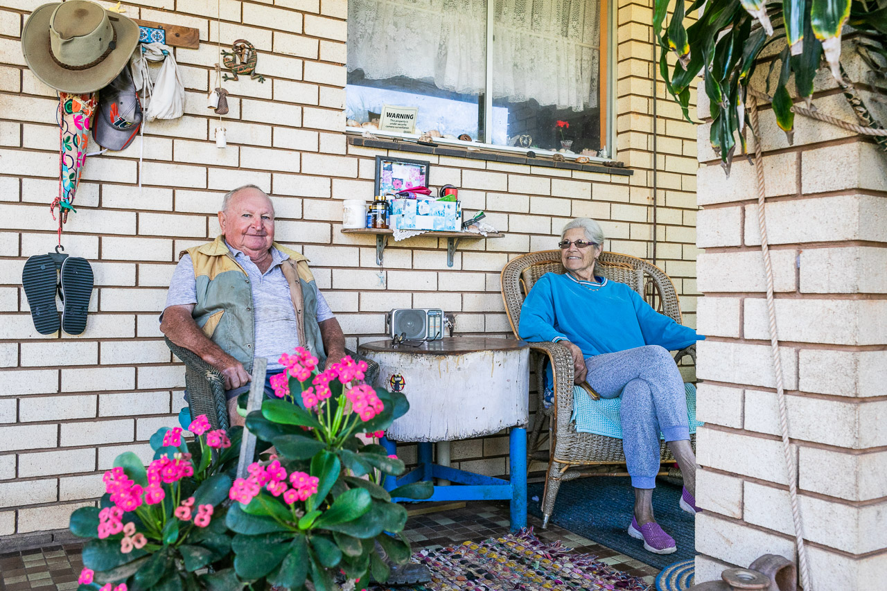 Old man and his wife sitting on their verandah surrounded by pot plants