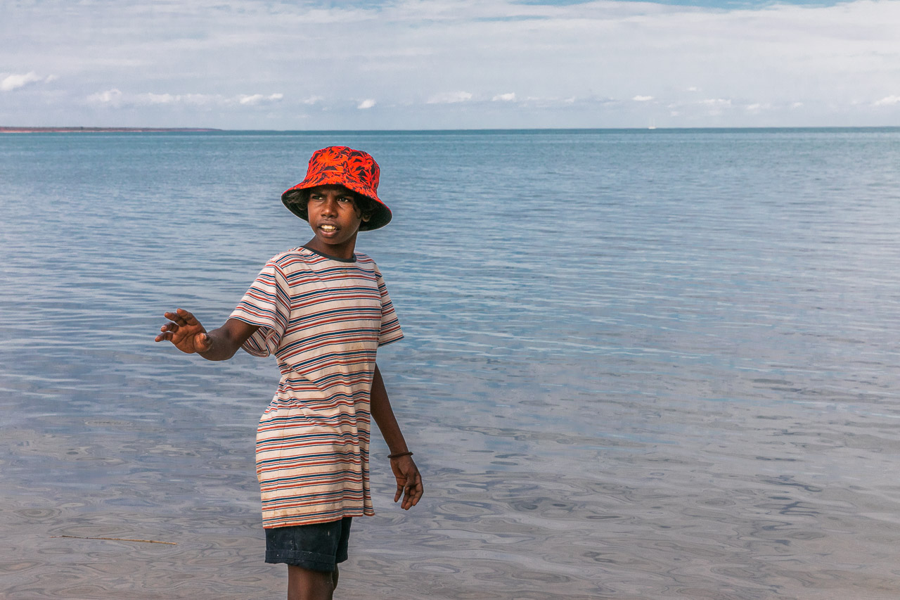 Indigenous boy in a red hat beside the ocean