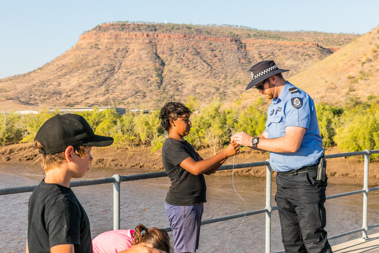 Police officer showing a boy how to put bait on his fishing line - this is community policing.