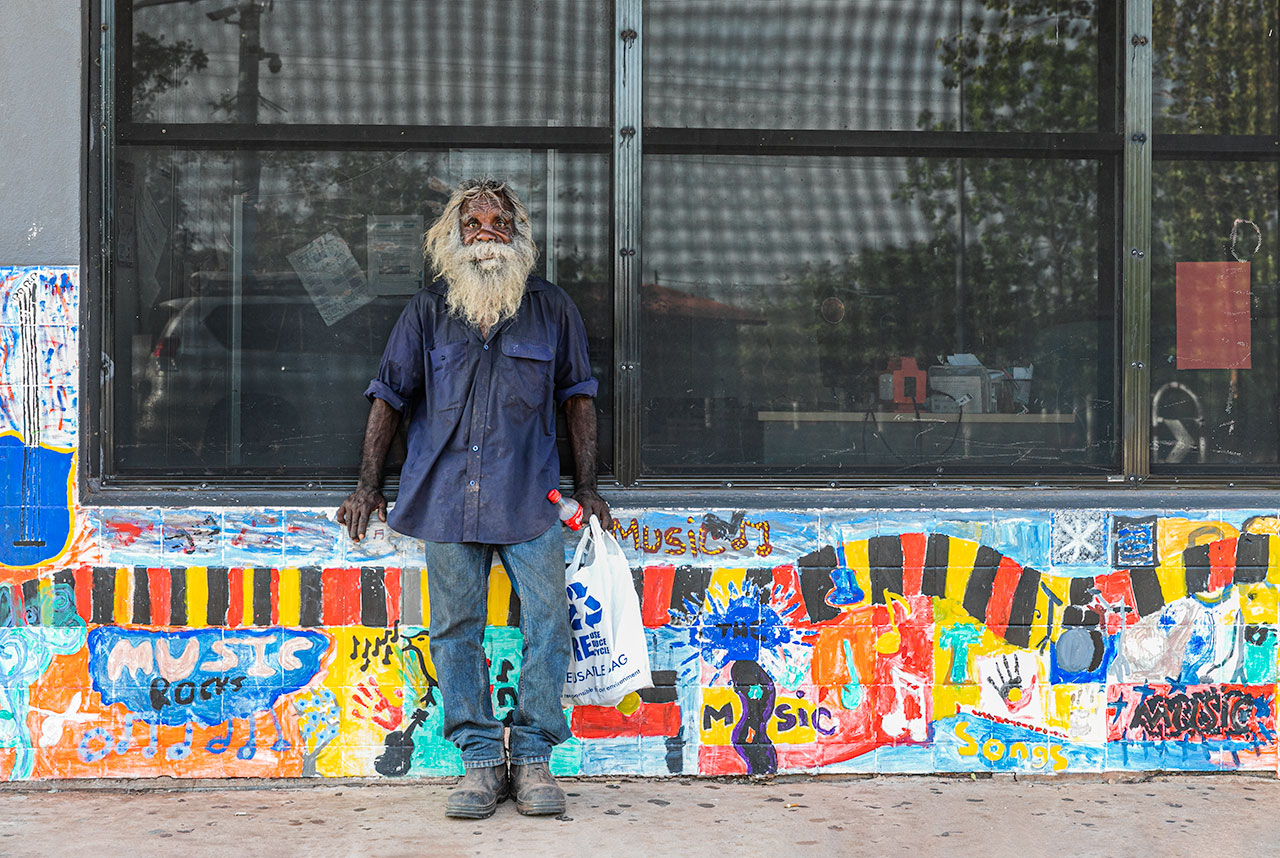 Aboriginal man standing in front of a shop with a brightly coloured wall