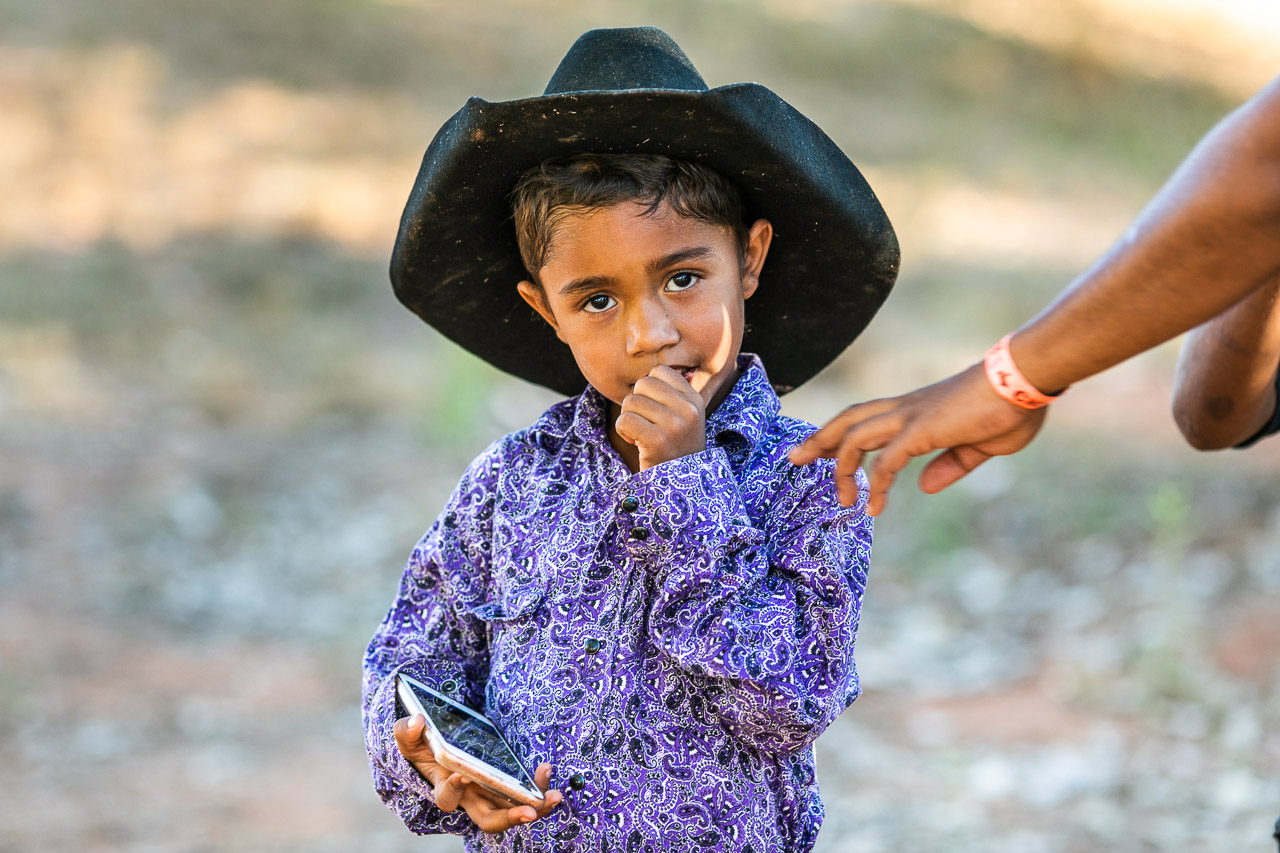Aboriginal boy with a bright shirt, a black cowboy hat and a smart phone