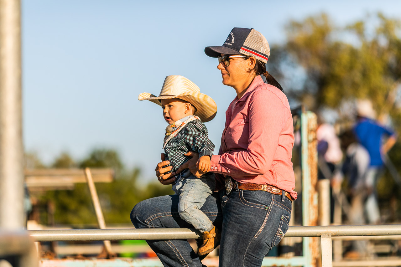 Baby dressed as a cowboy at the Broome Rodeo, sitting with his Mum on the railings