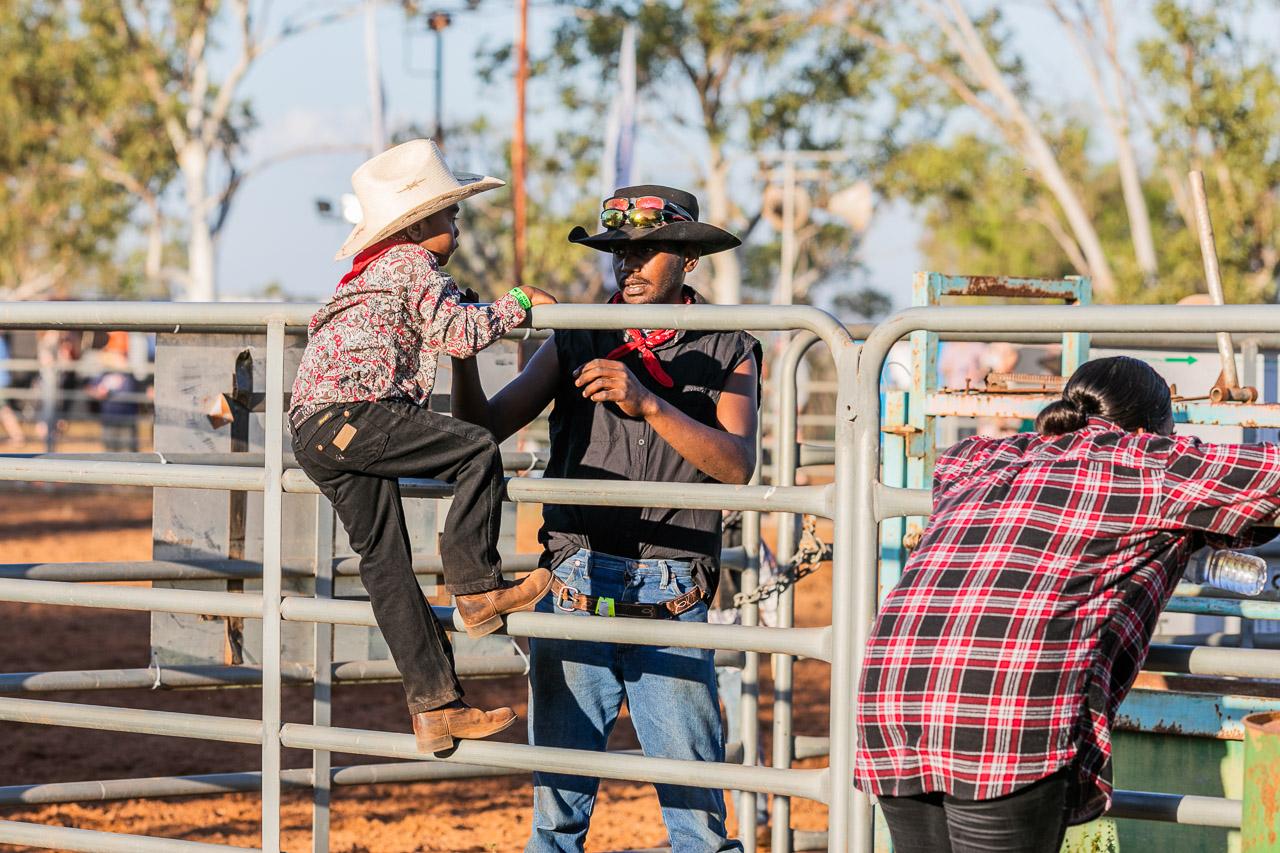 Man helping young boy climb over the railings at the Broome Rodeo