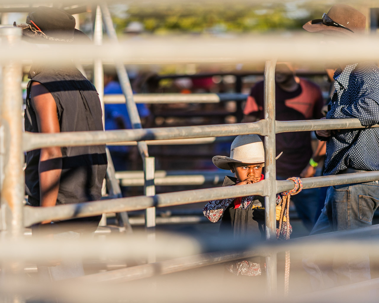 Young boy in a cowboy hat watching the adults through the railings at the Broome Rodeo