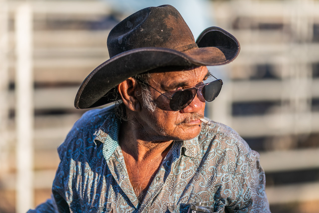 Old Aboriginal man wearing a cowboy hat and sunglasses, with a rollie cigarette in his mouth. Broome Rodeo 2019