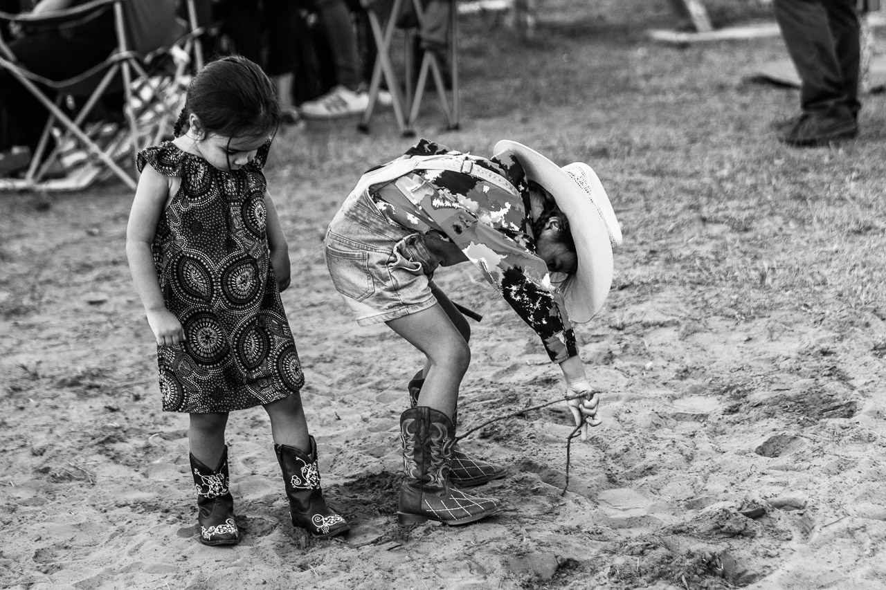 Young girl wearing cowboy boots and cowboy hat, drawing in the dirt at the Broome Rodeo