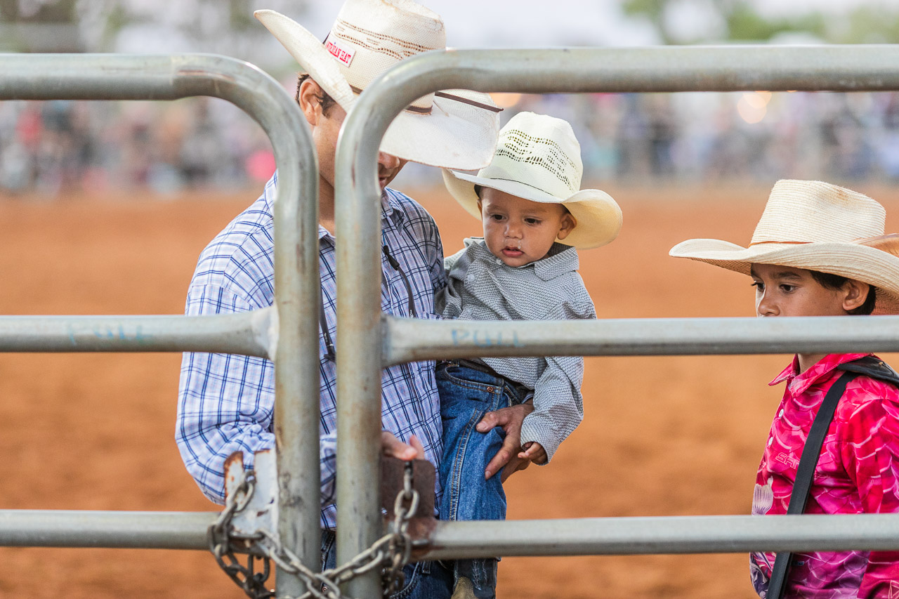 A father opens the metal gate at the Broome Rodeo, watched by his two children 