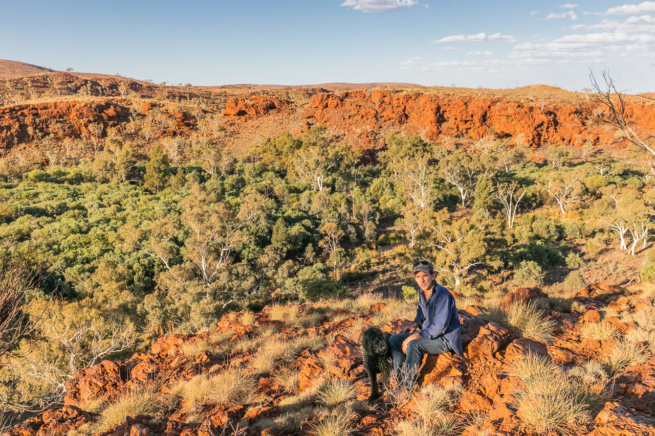 A man and his black dog in the Pilbara, amongst native flora and red rocks