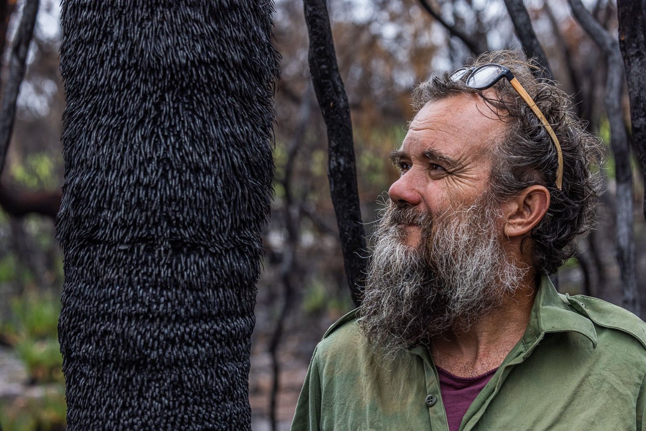 Bearded man next to the burnt trunk of a Kingia following a bushfire