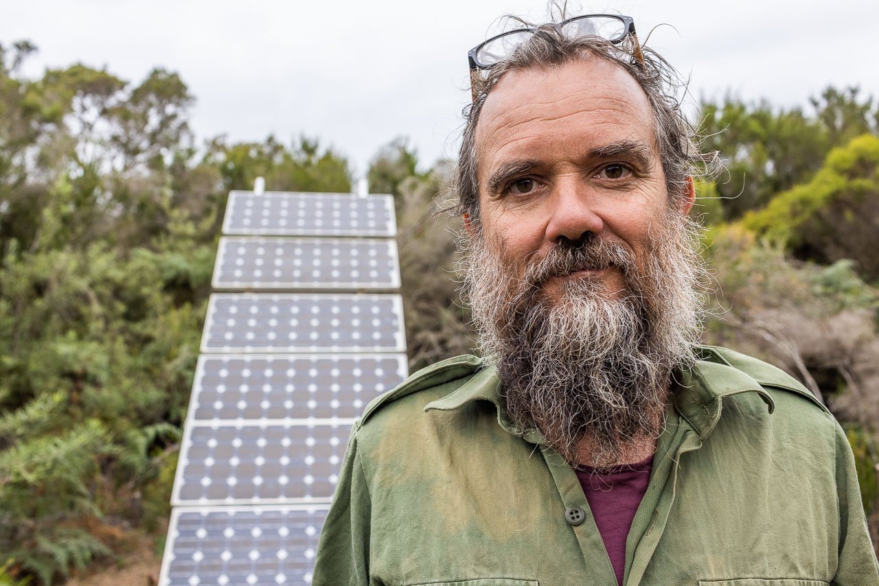 Bearded man in front of a bank of solar panels in the bush