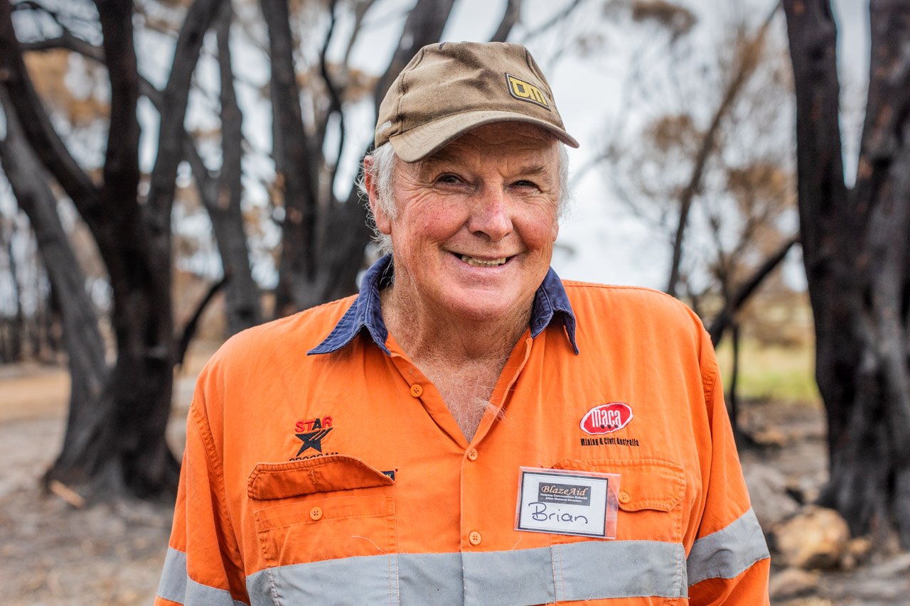 BlazeAid volunteer in front of burnt trees