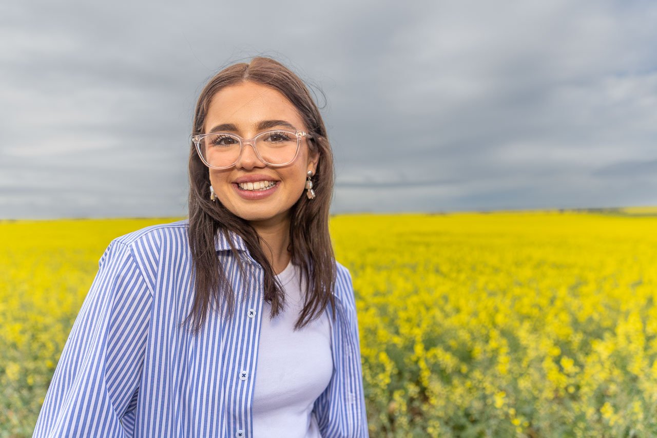 Young woman in a blue shirt in front of yellow canola paddock