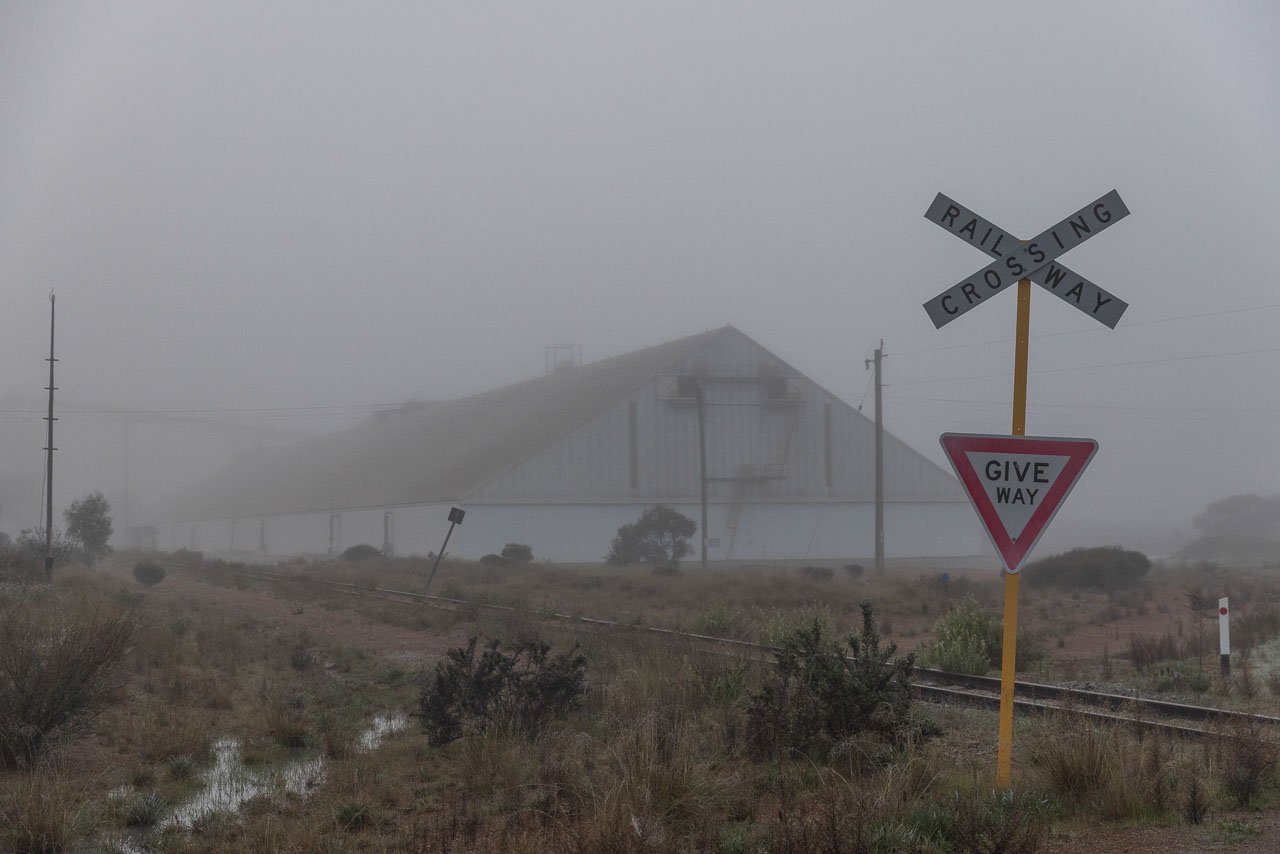 The railway crossing stop sign on a foggy morning, with the Kulin grain bin behind