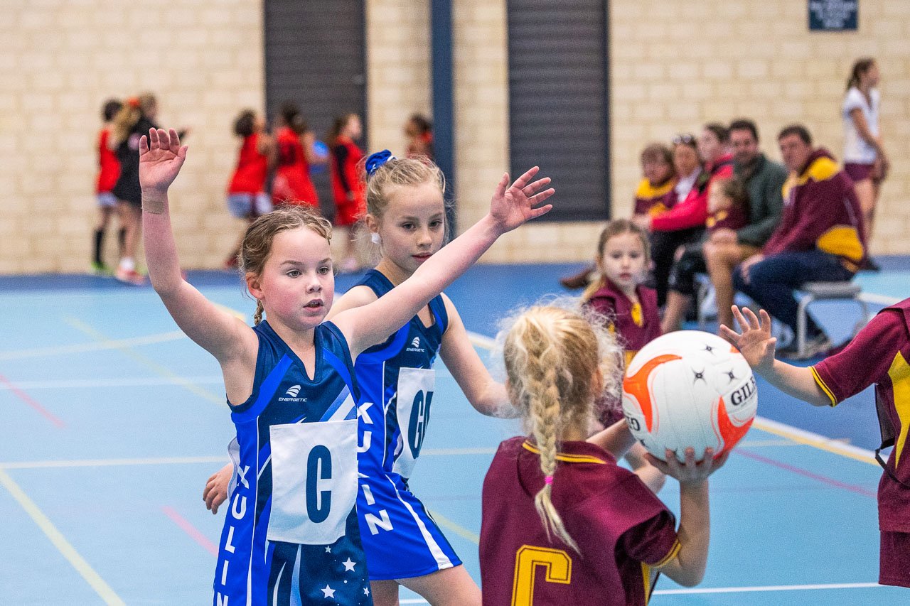 A junior netball game on an indoor court