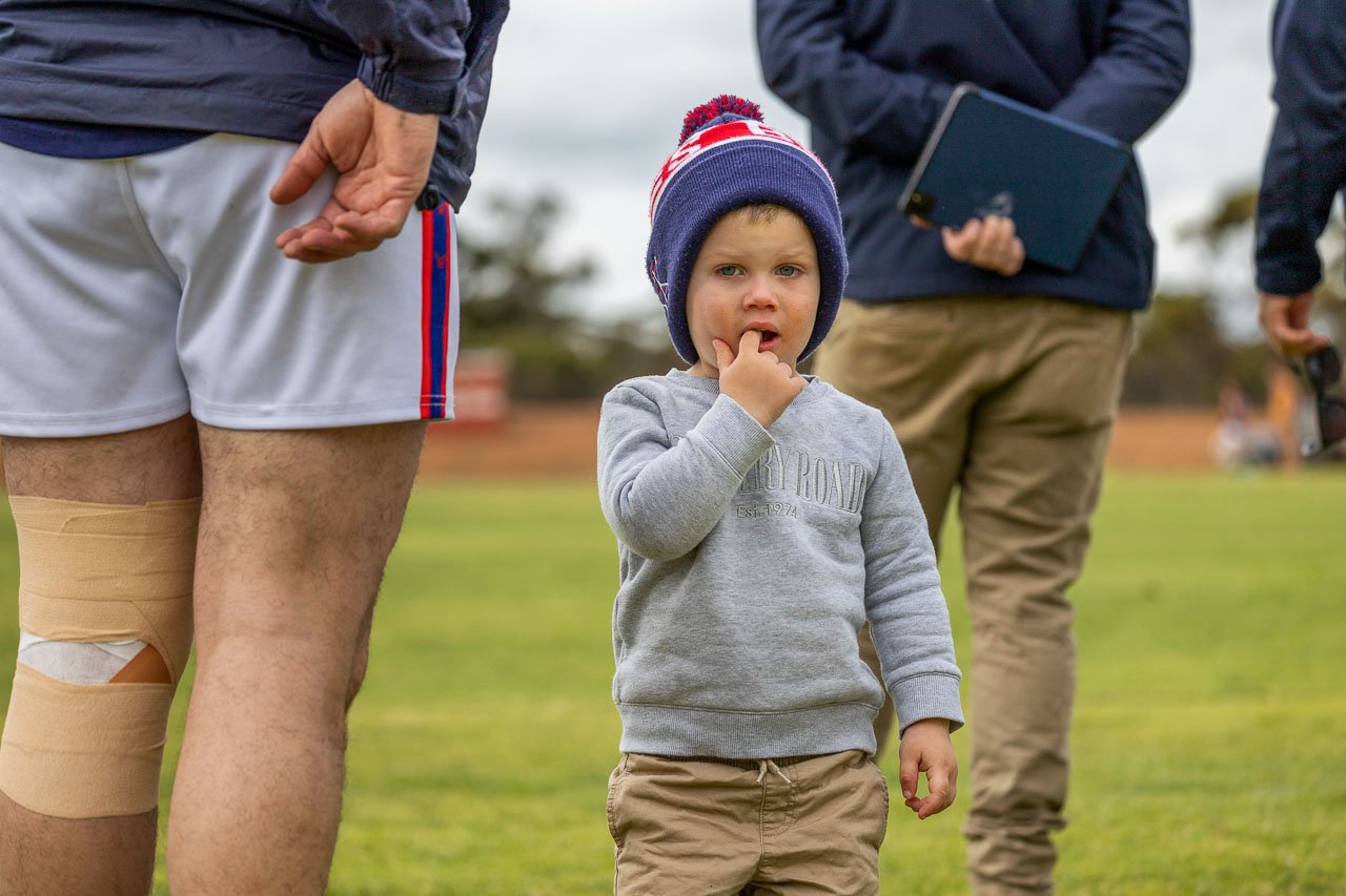 Young boy in a bobble hat beanie on the sidelines of the football field
