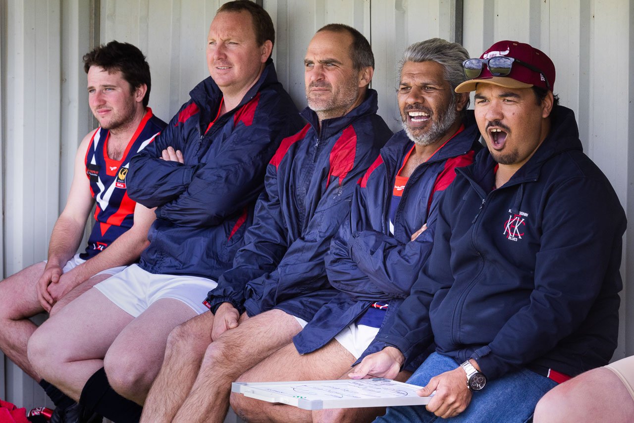 The coach and team mates shout encouragement from the sidelines during an Aussie Rules footy match