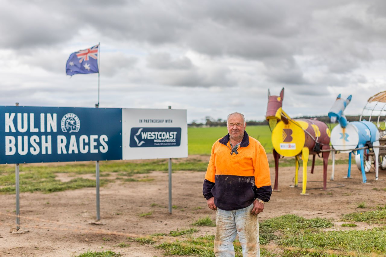 Portrait of Serge Lucchesi in front of the Kulin Bush Races sign and one of the Tin Horse Highway sculptures. The annual Kulin Bush Races take place on the Lucchesi's farm