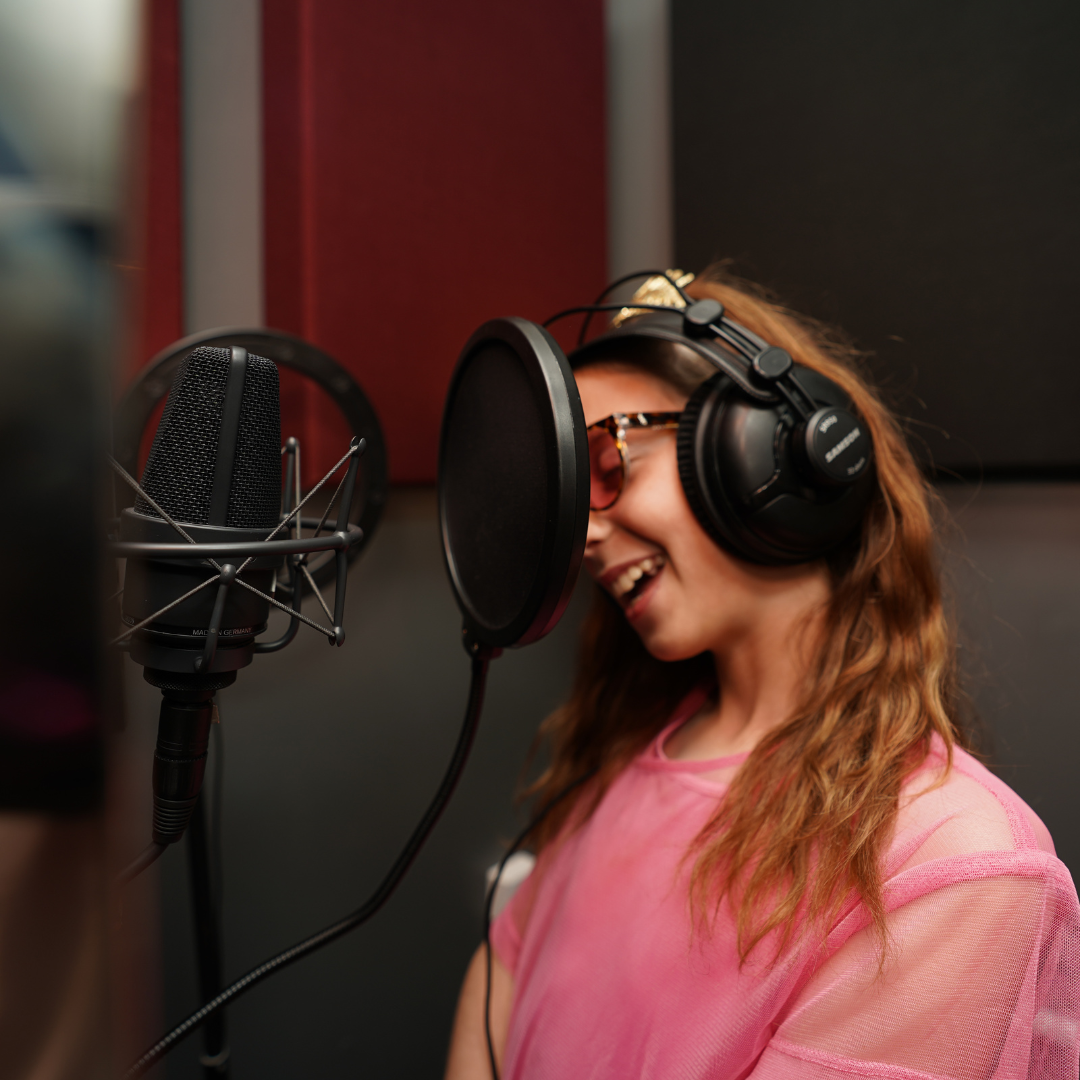 Woman in pink shirt recording vocals with headphones and microphone in a studio.