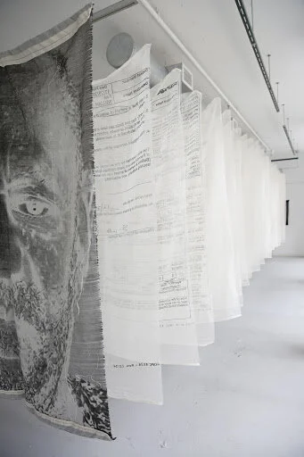 Image: Alex Younger, Litigious , 20 document title pages from Constand v. Cosby, full 3 page Criminal complaint for the People of the Commonwealth of Pennsylvania v. Cosby, and Bill Cosby's mugshot on 23 screenprinted cotton cheesecloth panels and 1 jacquard-woven cotton panel, 42in x 60in each, 25ft long installed. Photo: Alex Younger.