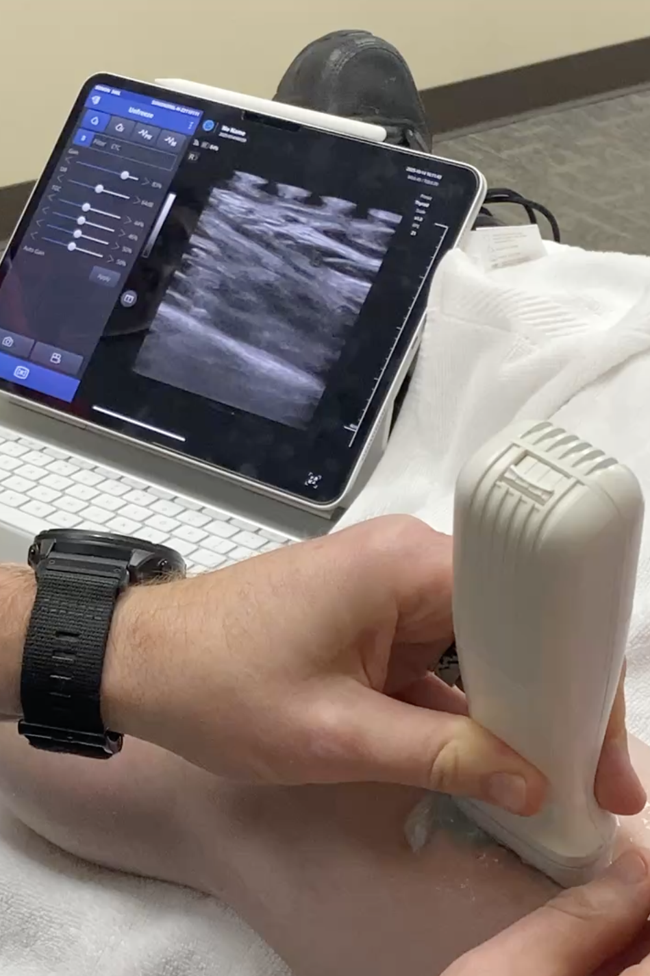 A medical professional uses an ultrasound device to examine a patient's knee while viewing the ultrasound images on a tablet screen.