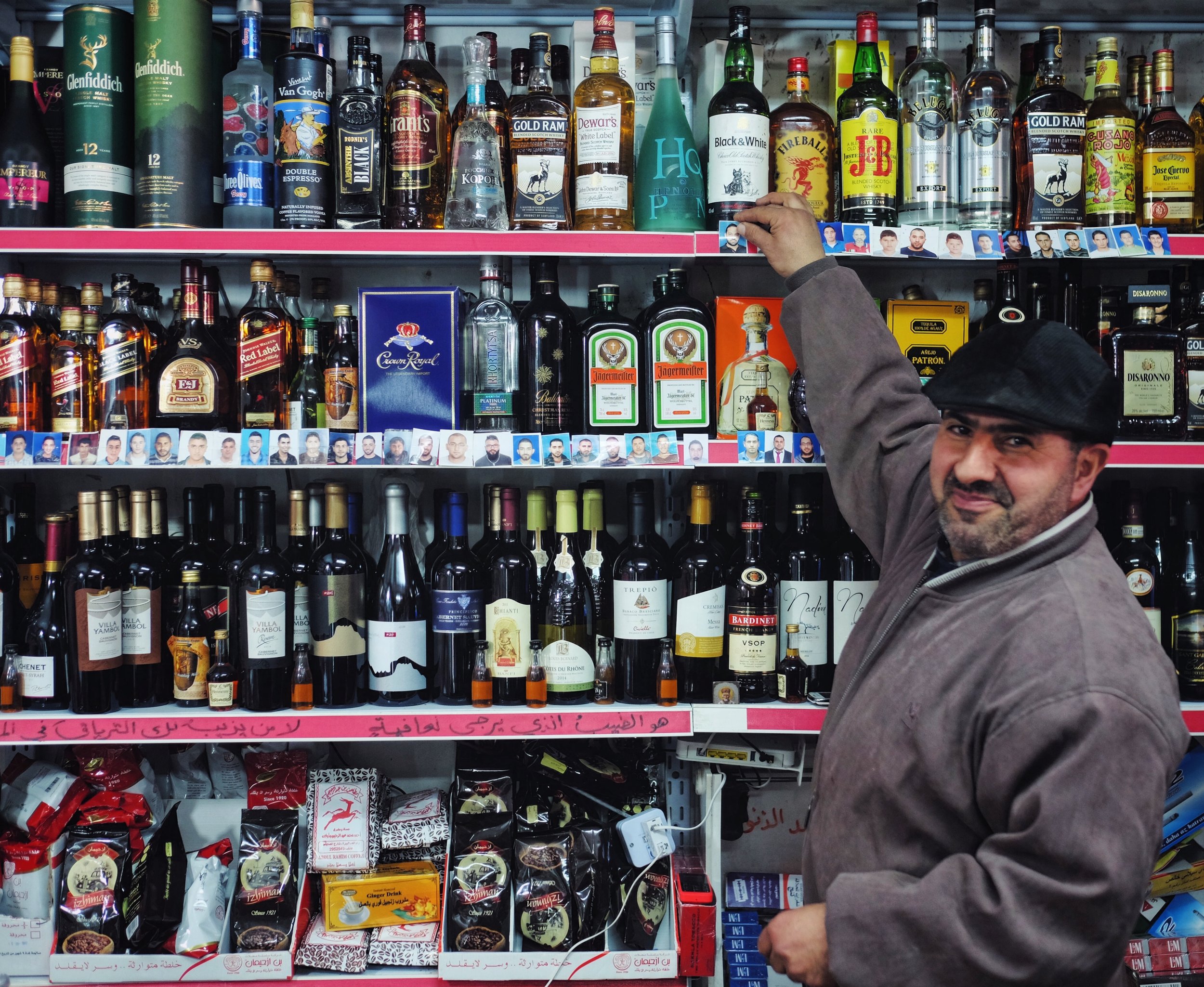  A West Bank liquor store, but if you look closer you'll see boys' passport photos lining the shelves. The boys in Taybeh want to go to America so they bring their pics to Sarri, a US citizen and owner of this shop. He moves the pictures from the bot