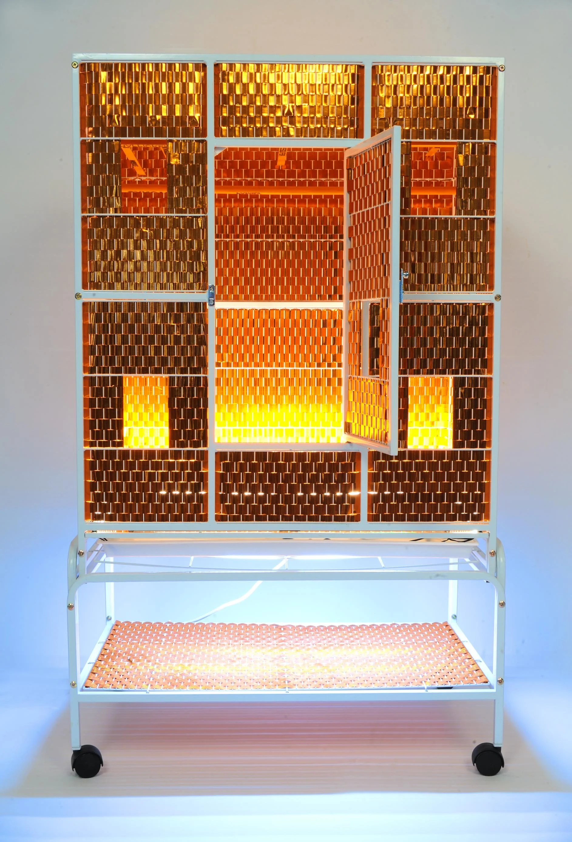 Orange Cage - Immigrant Loops | 2018 | 31 1/2" L by 19" W by 53 3/4" H |. White steel cage, orange iridescent ribbon, adhesive, mirror, wood rods, vinyl black letters, and LED lights