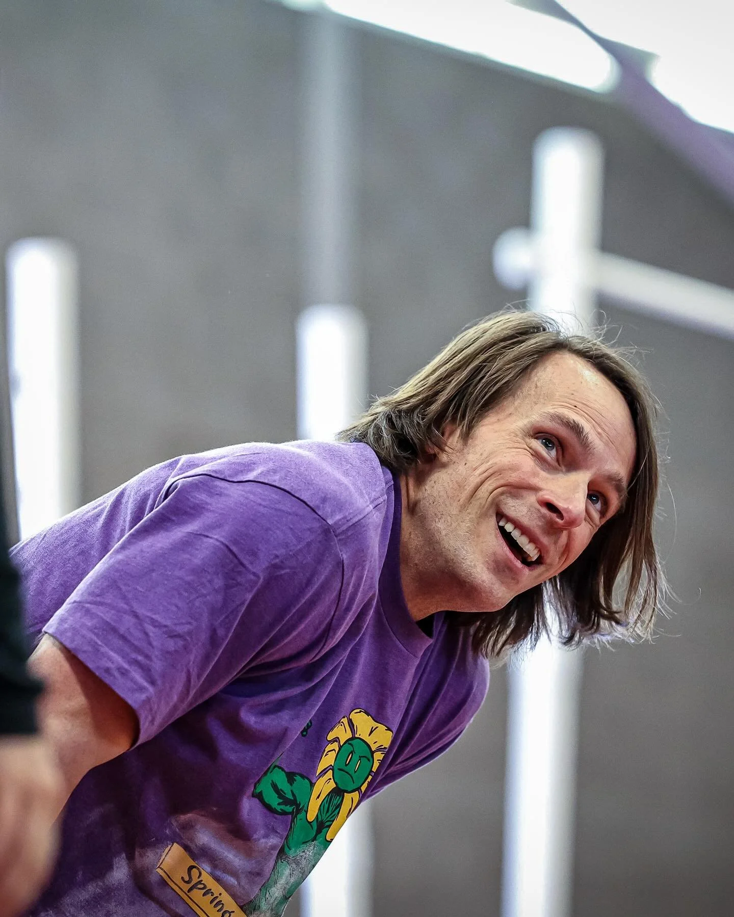 CrossFit Hopkins nutrition coach smiling and leaning forward, wearing a purple T-shirt with a cartoon sunflower design.