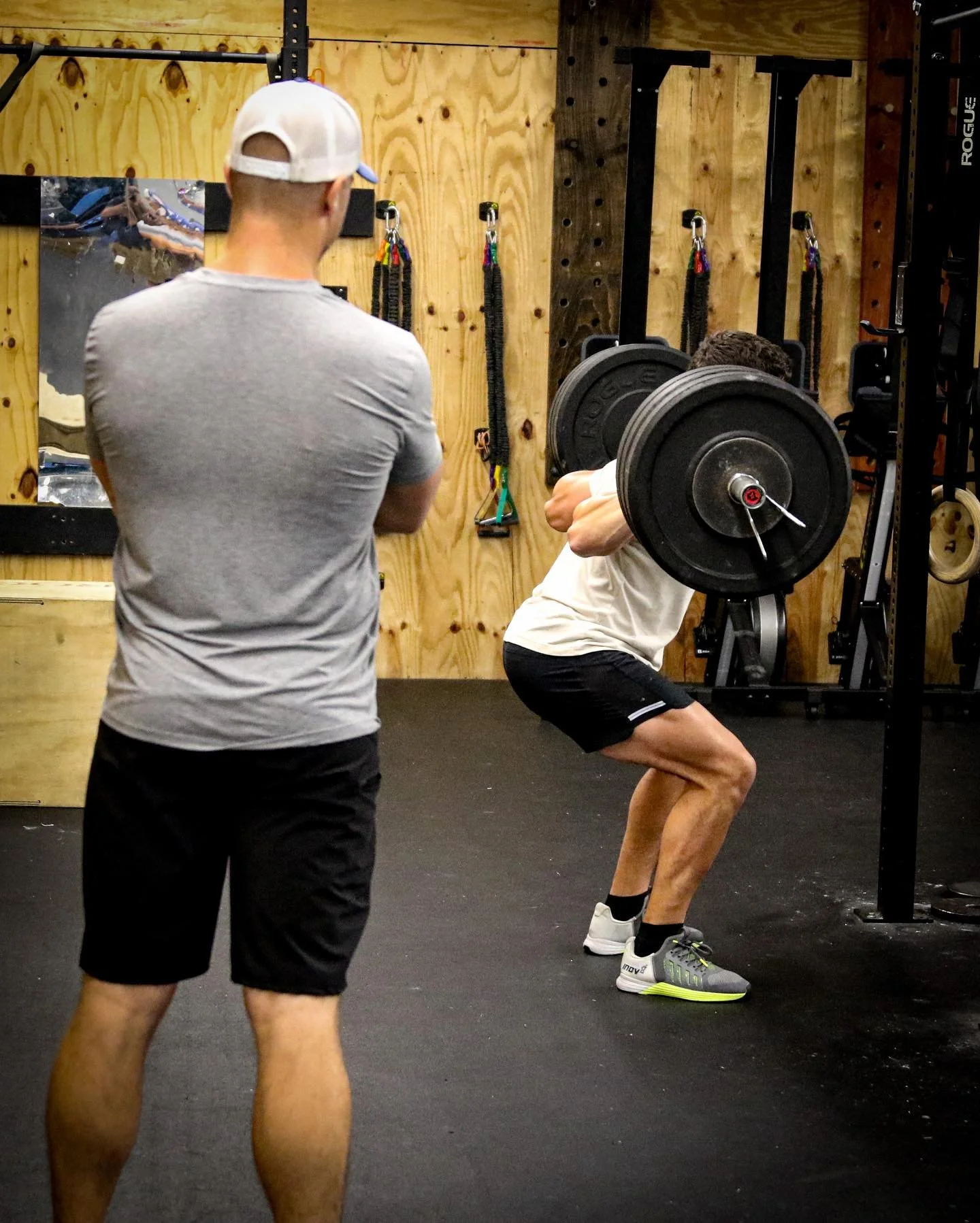 Photo of a male athlete back squatting while a male coach observes technique