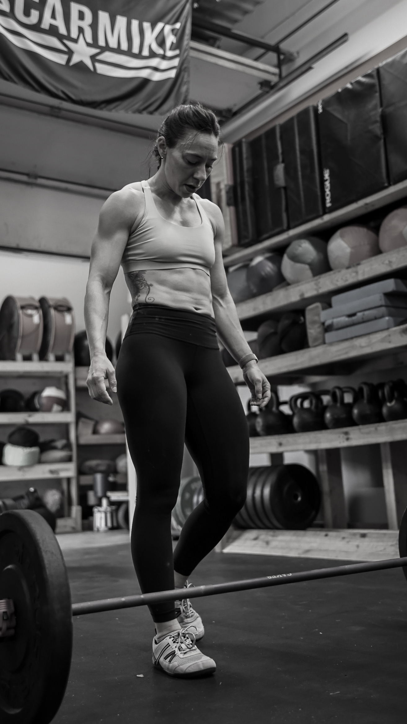 Black and white photo of a woman in a CrossFit gym standing in front of a barbell