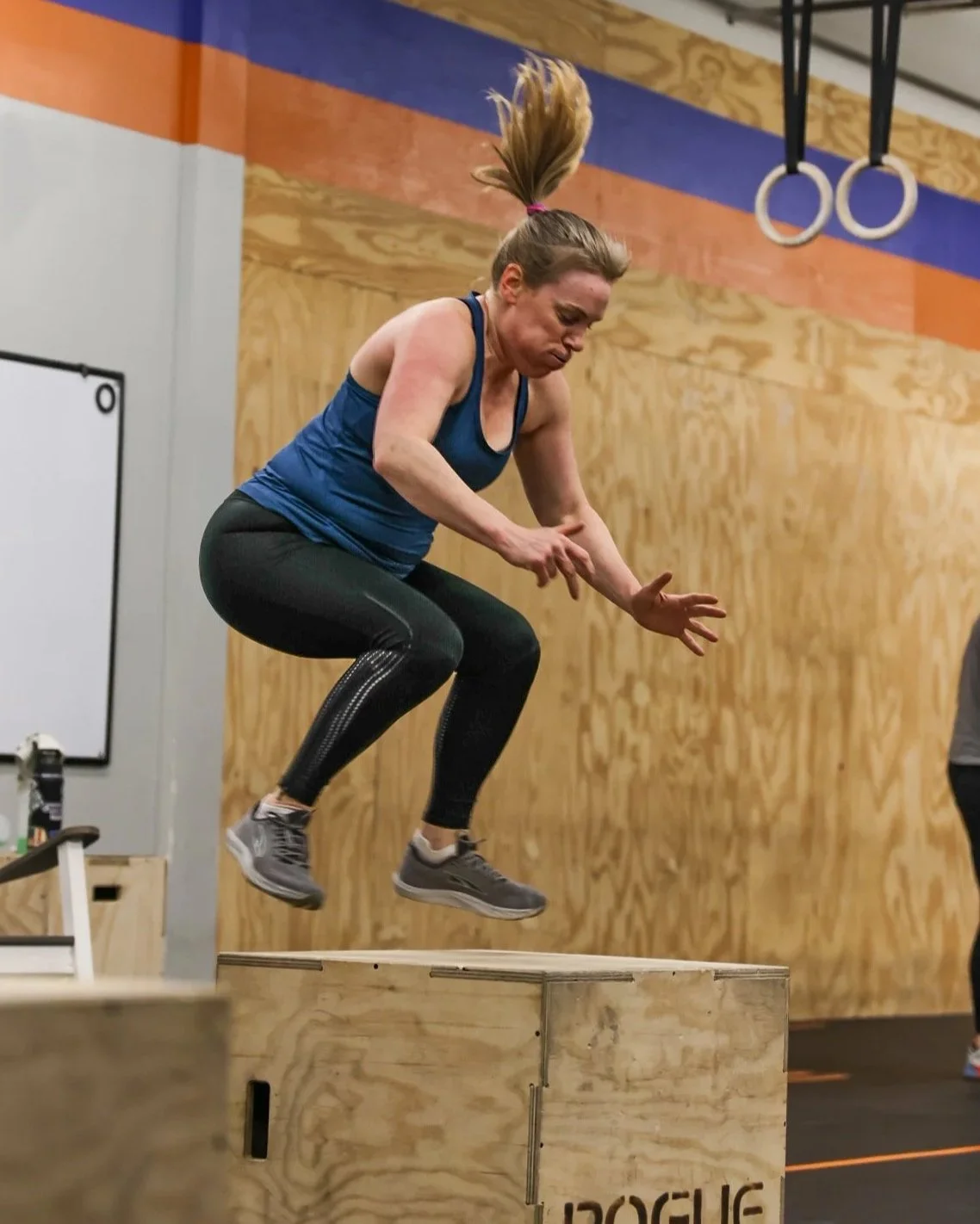 Photo of a woman in workout clothes jumping up onto a wooden plyo box at CrossFit Hopkins