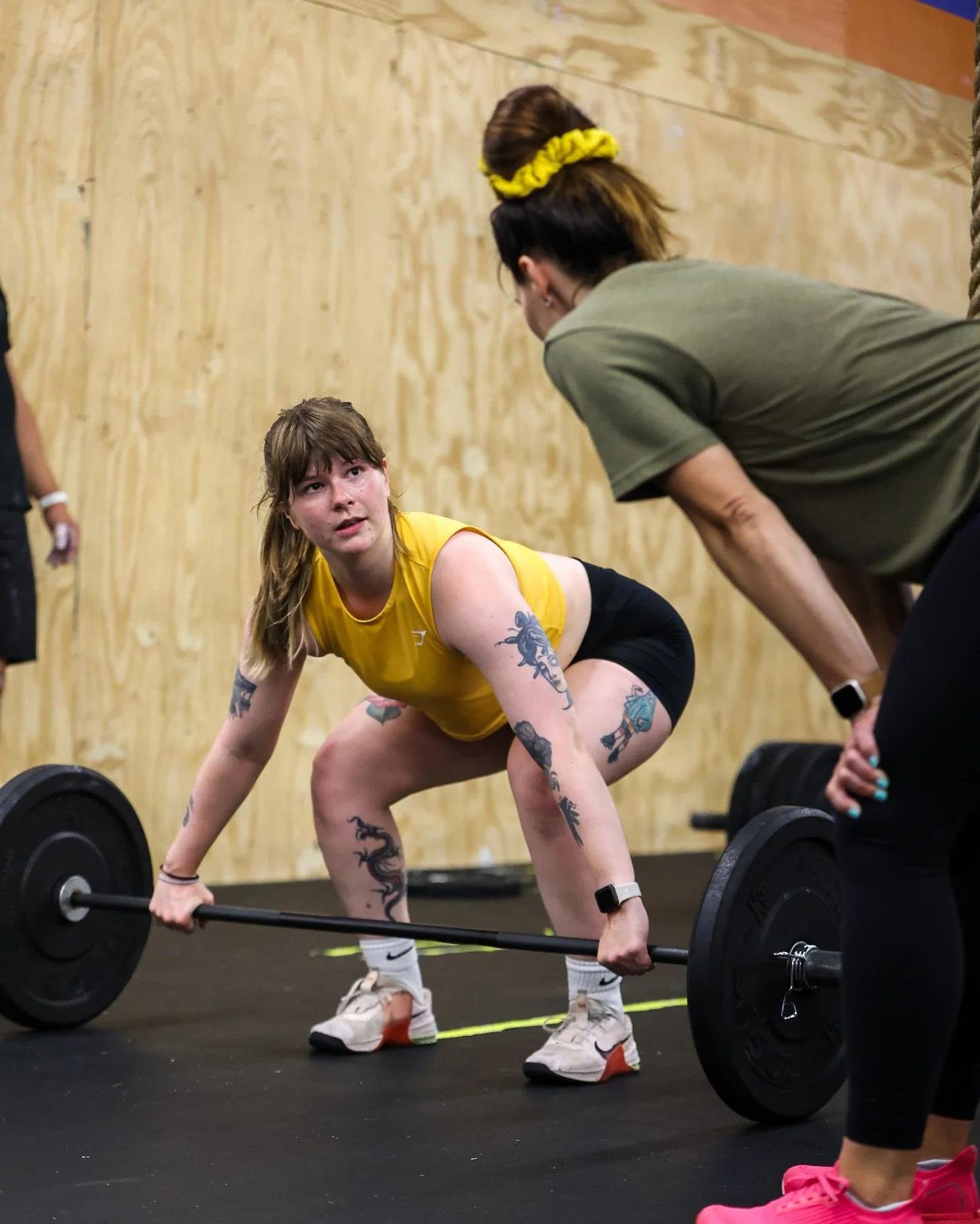 Photo of a female athlete in a ready position at a barbell listening to a female coach giving cues