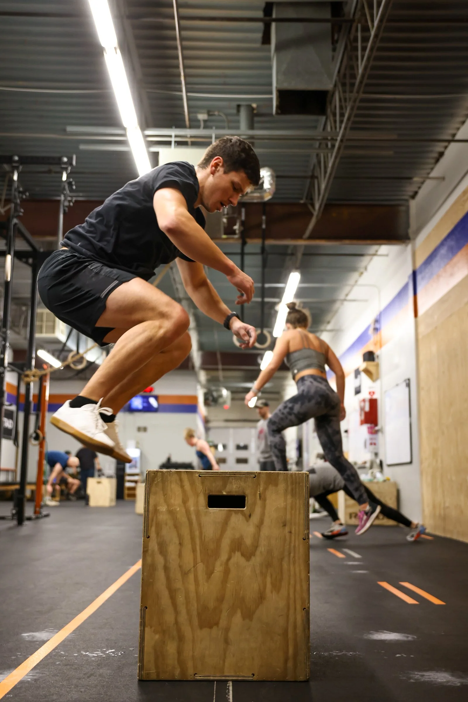 Man mid-air while jumping on a wooden box in a workout
