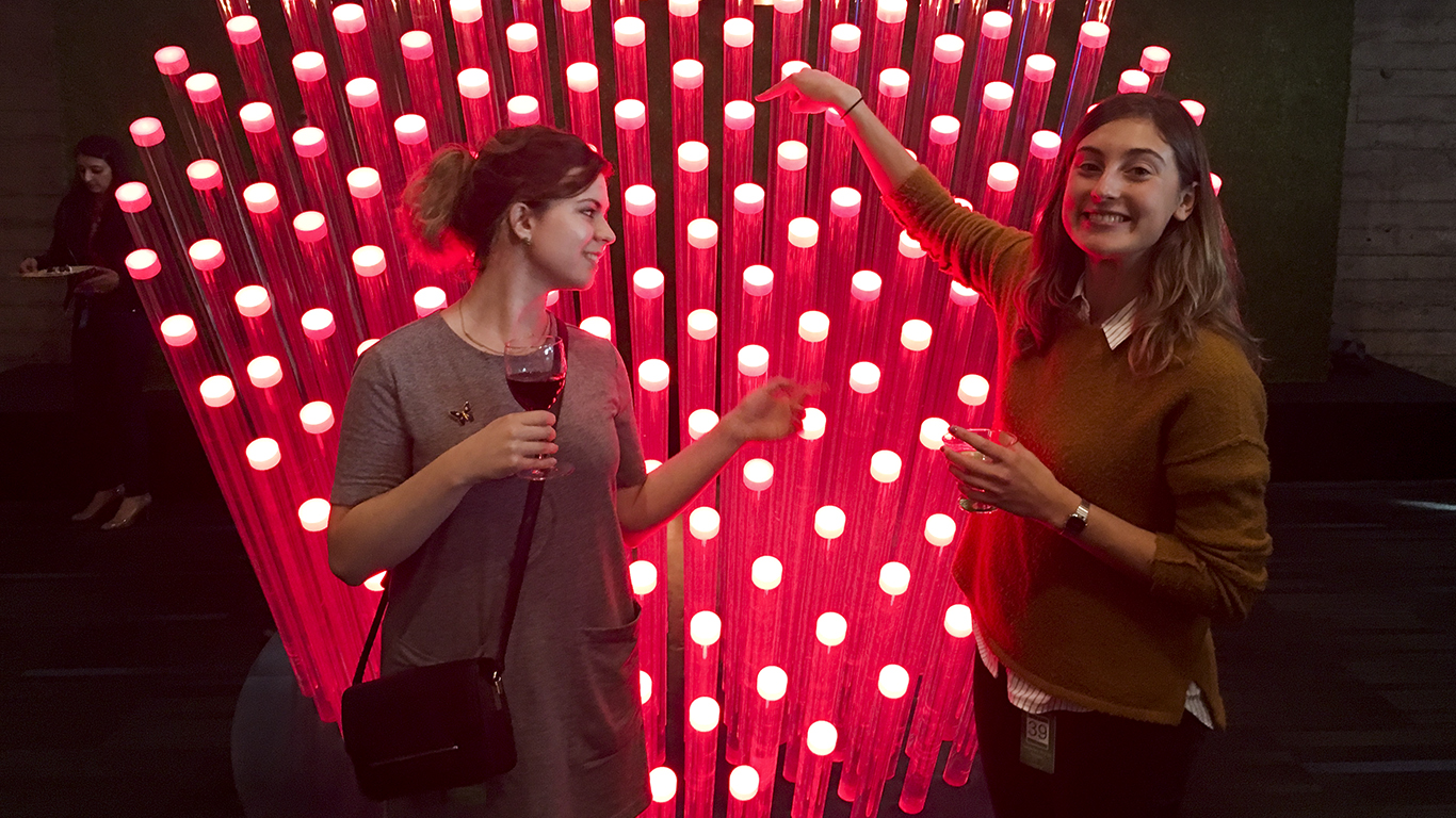 Two women stand in front of a large heart made of frosted acrylic tubes, each glowing with a red light.