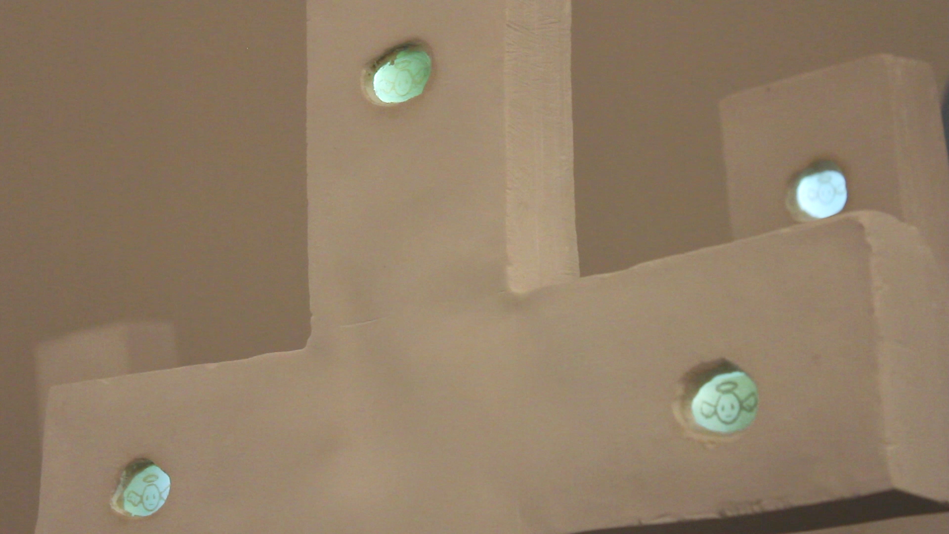 A close up of a plaster cross with three LCD screens depicting pixelated angel creatures.