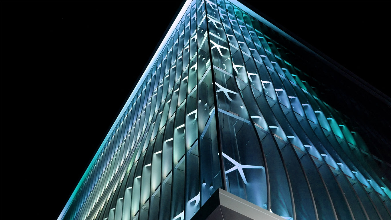 The corner of the parking garage rises up in an imposing way, glowing with a sea green and blue light.