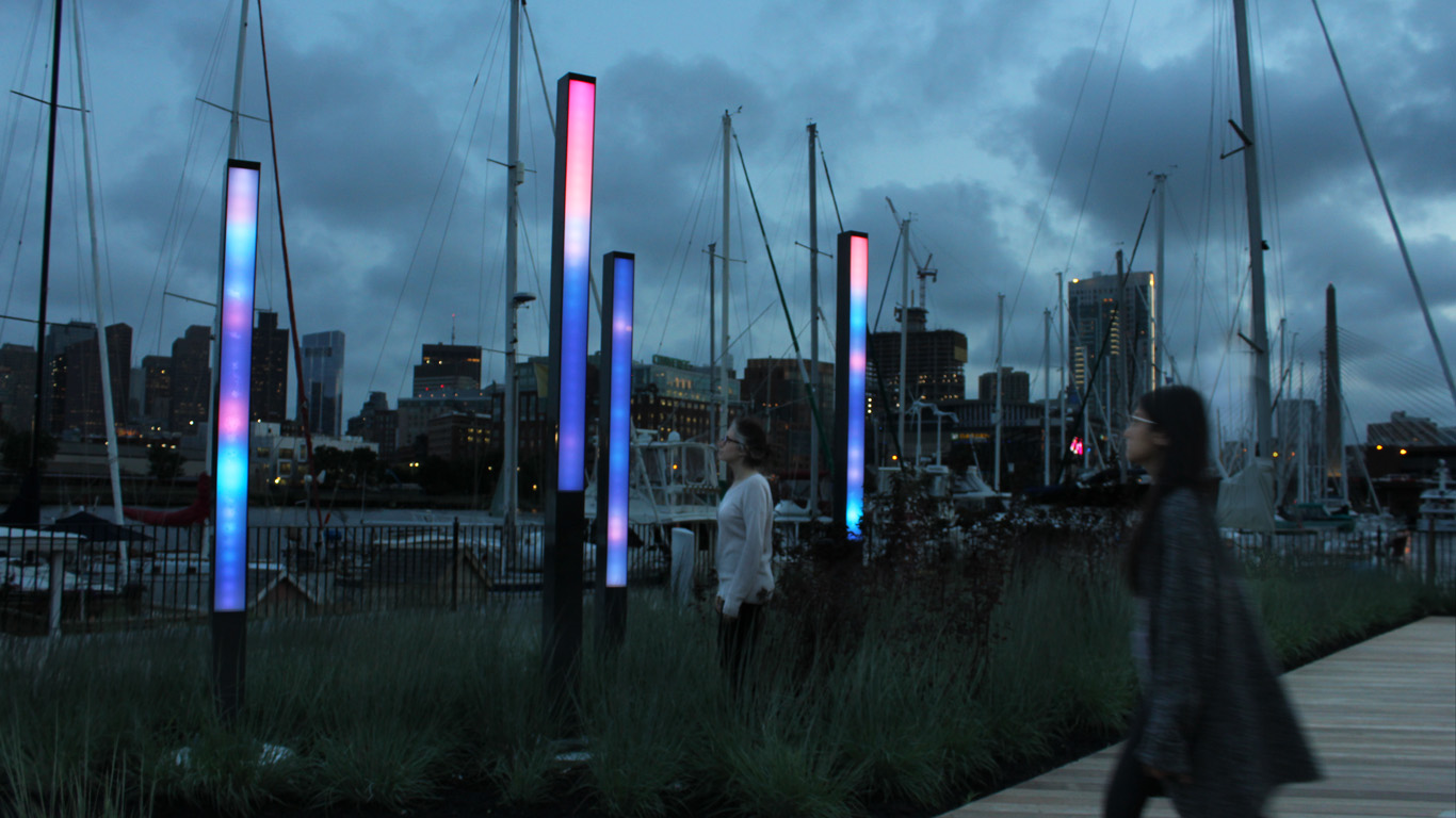 Four illuminated columns in front of a harbor with boats display the current wave conditions in lights.