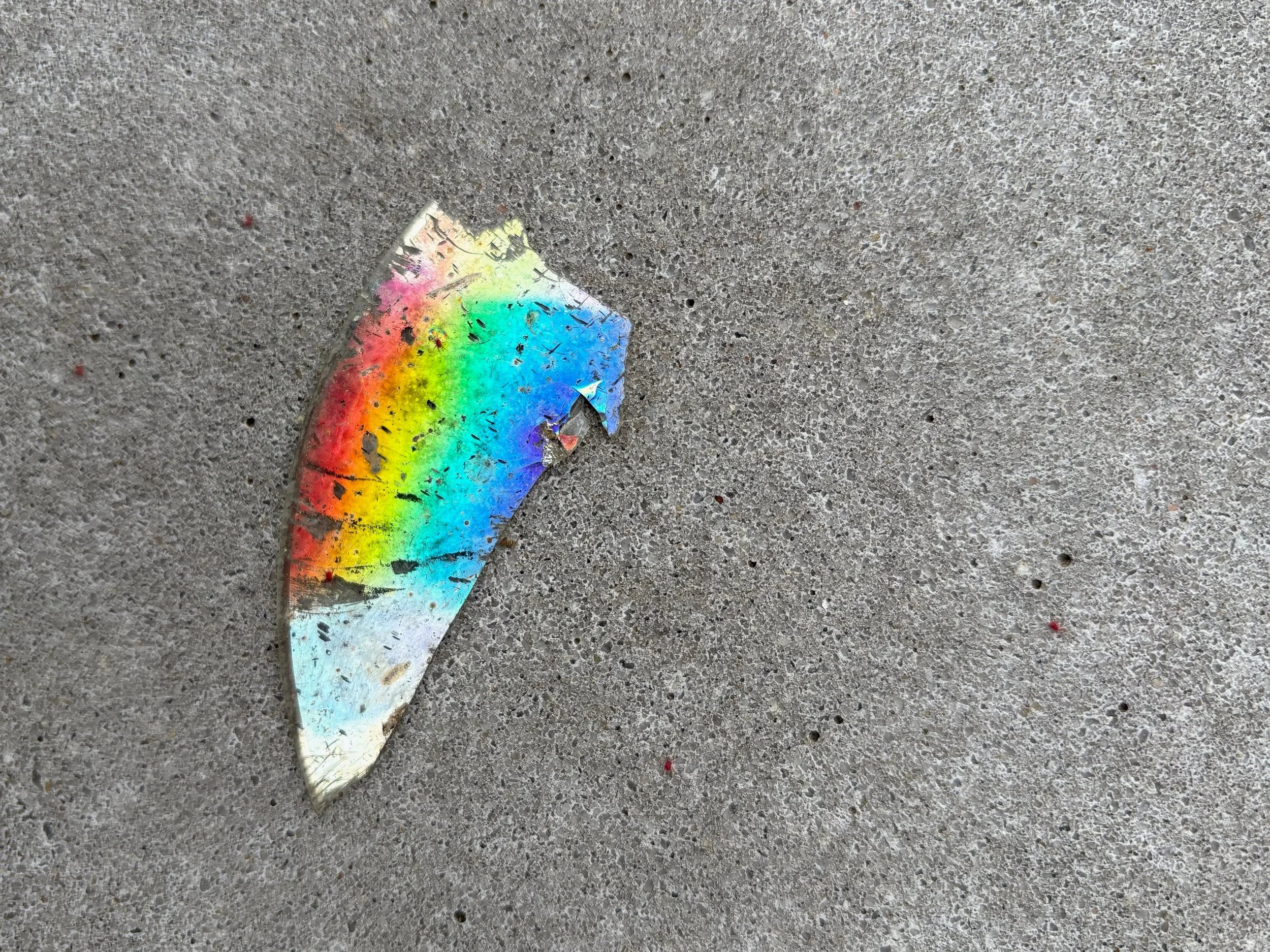 A photo of a rainbow shard of a CD on a concrete surface.