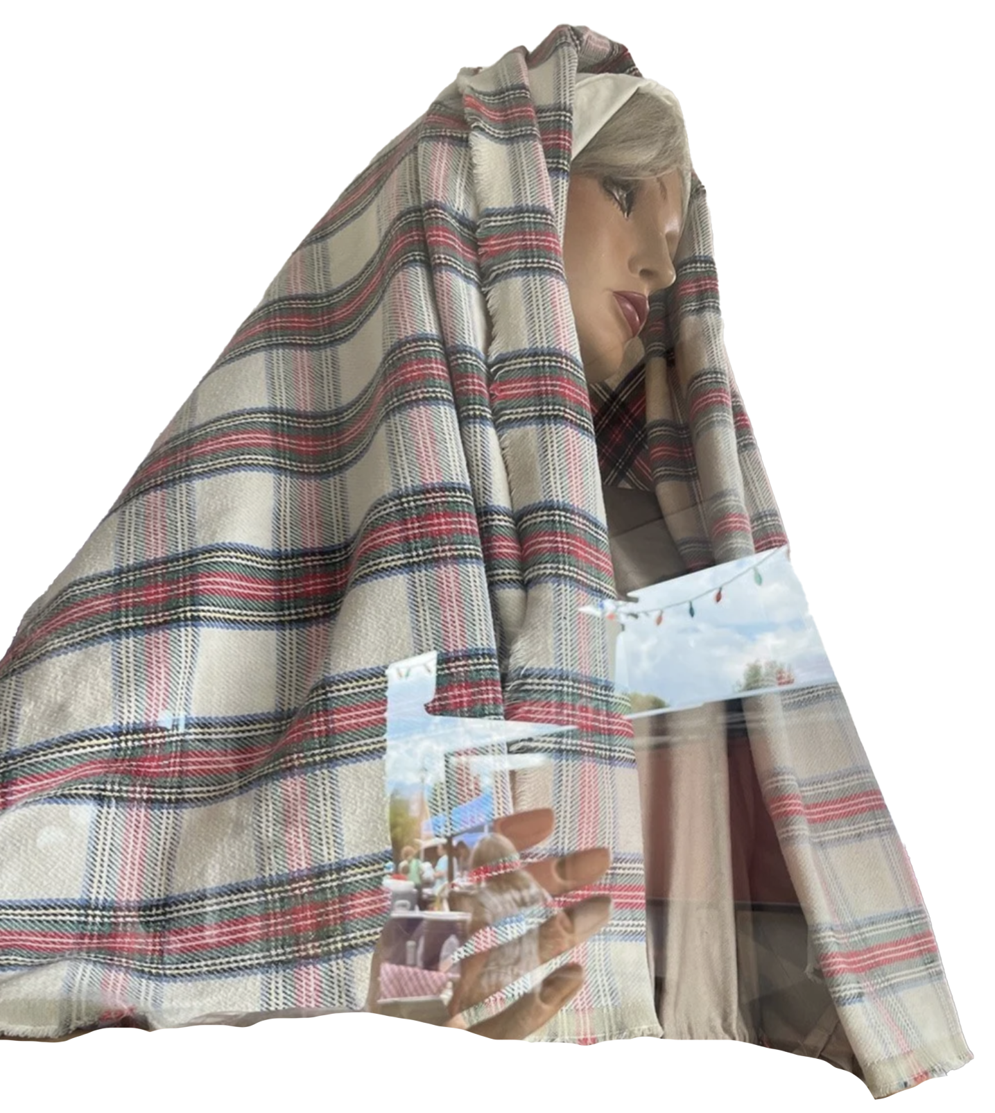 A mannequin wearing a plaid shawl, is seen through a store window with holiday decorations against a transparent background