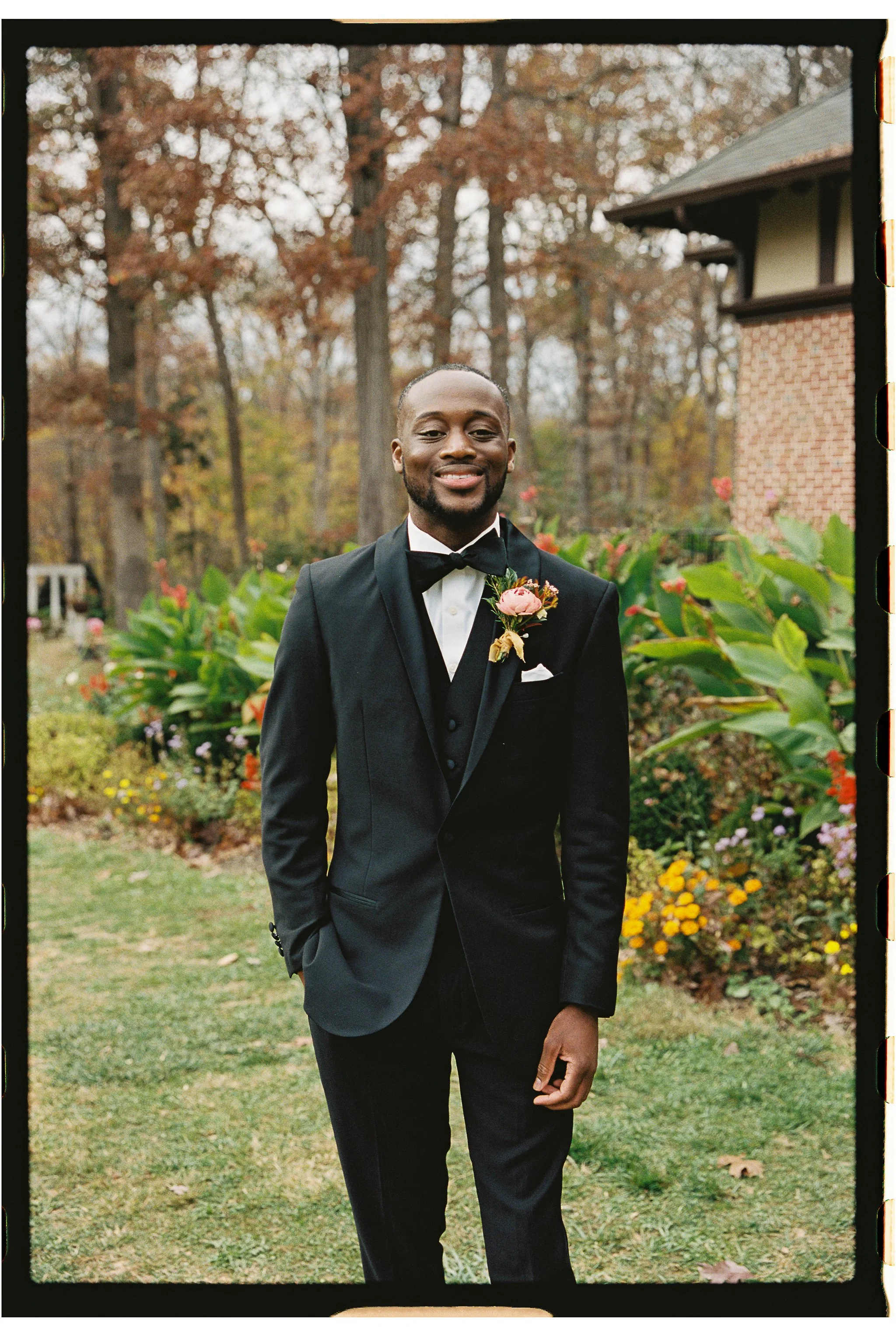 Man in a suit standing outdoors with a forest and flowerbed background. gramercy mansion maryland wedding