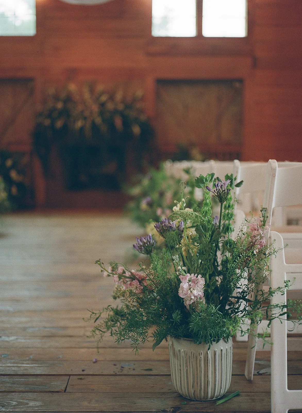 A bouquet of flowers in a white vase sitting on a wooden table in a room with wooden walls and windows. ocracoke outerbanks wedding film photographer