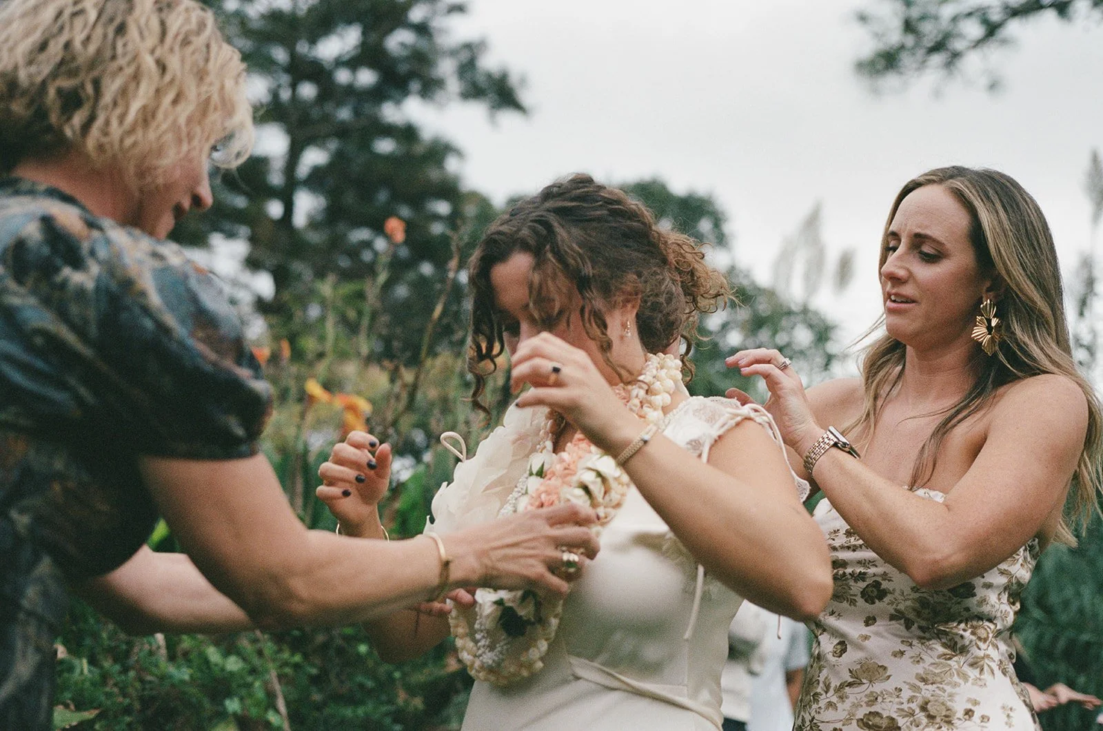 Women putting a flower lei on a bride during a wedding ceremony outdoors ocracoke outerbanks wedding film photographer
