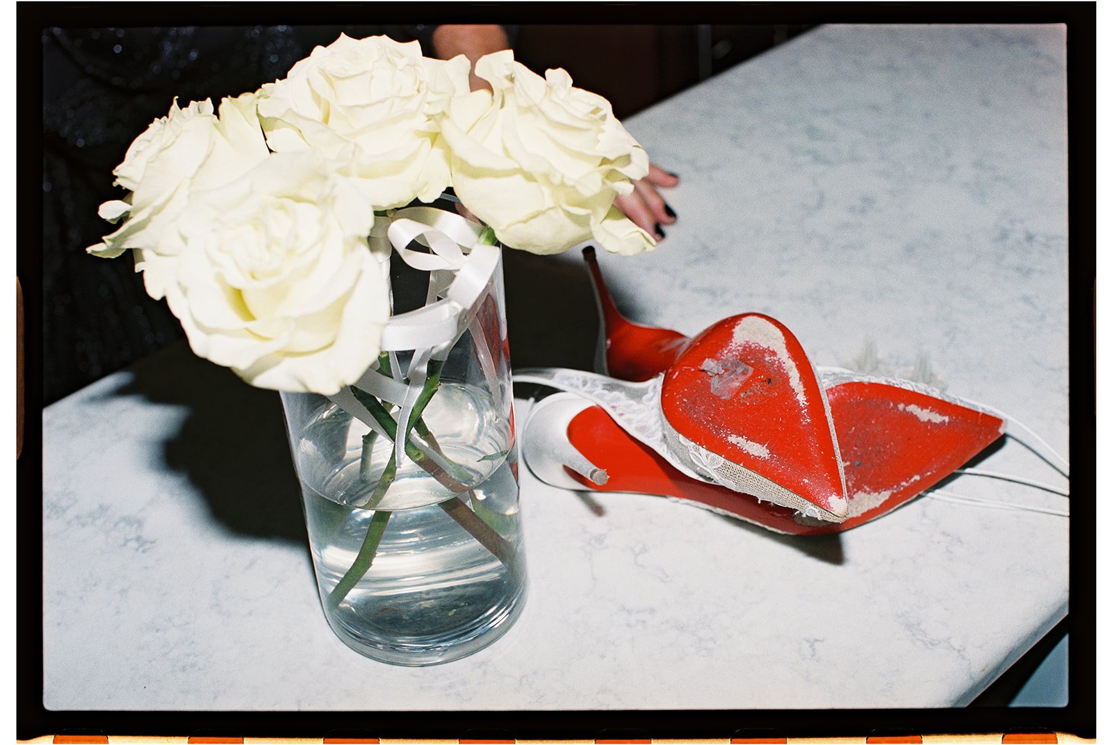 A clear glass vase with white roses on a white surface, with a red heart-shaped object and white lace in the background. roanoke wedding film photographer virginia