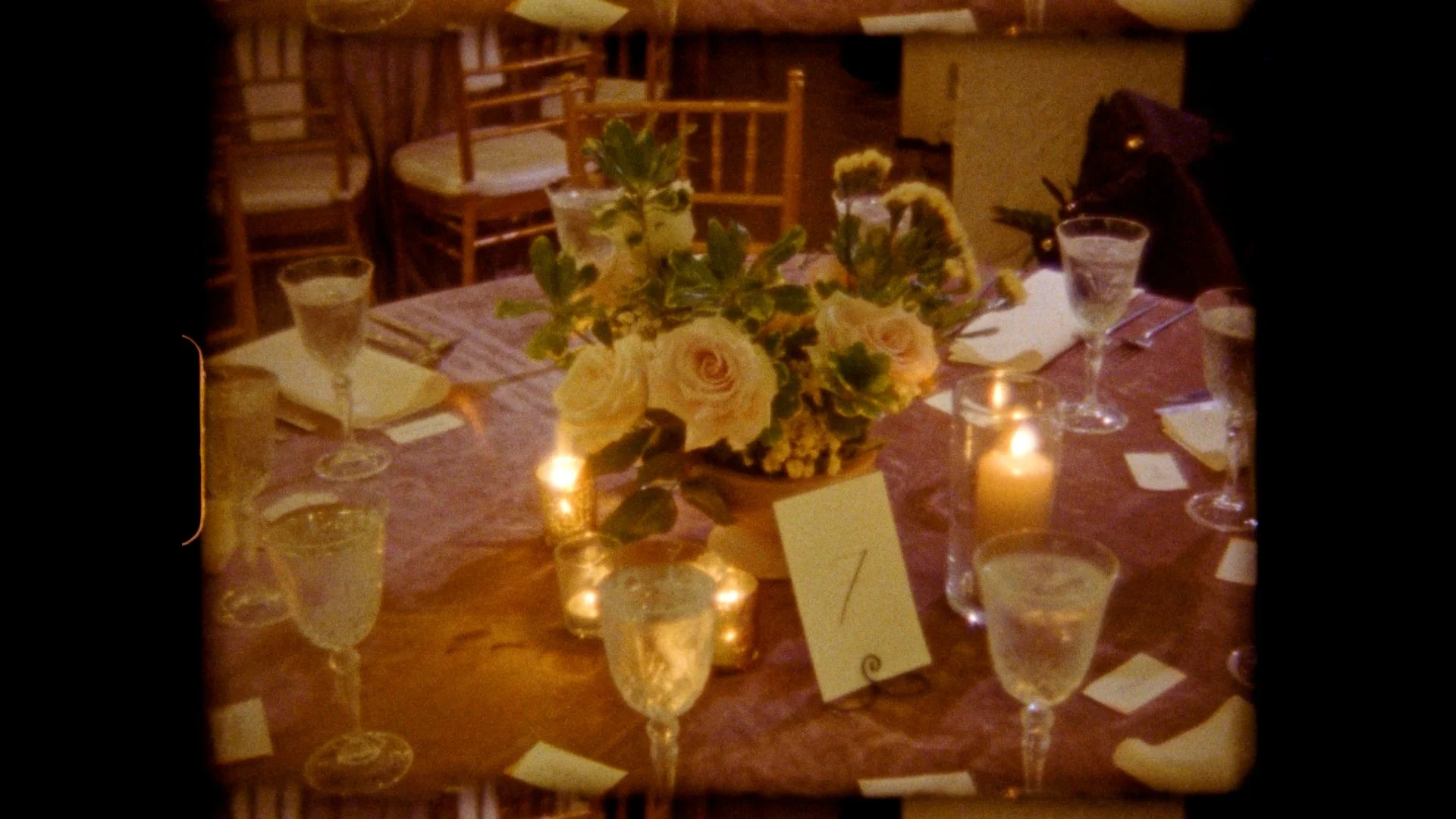 Table set for a formal event with floral centerpiece, candles, glassware, and place settings. Super8 film