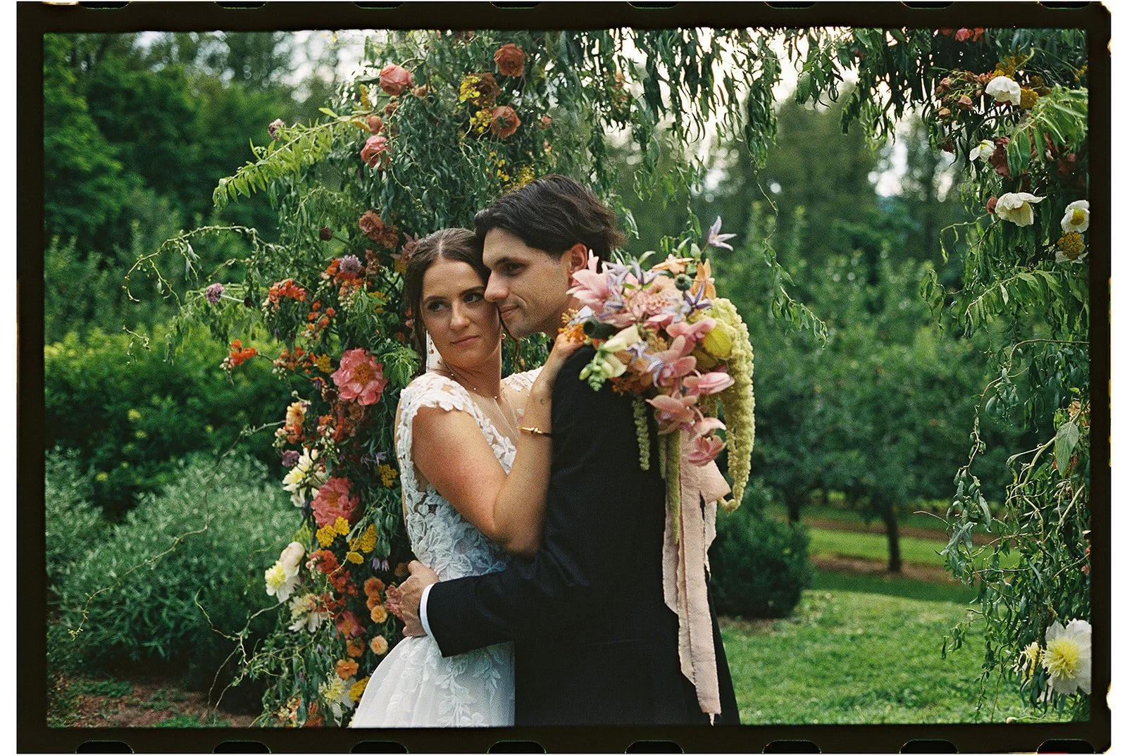 A couple on their wedding day, embracing under a floral arch in an outdoor garden setting. charlottesville virginia wedding photographer eastwood winery