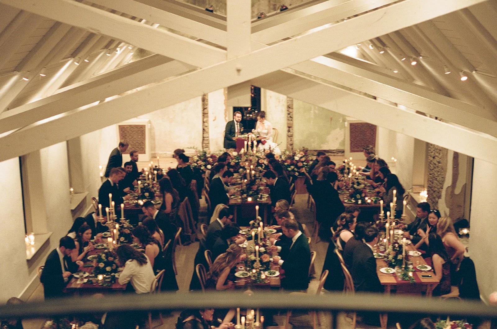 A large formal dinner event with many guests seated at tables decorated with flowers and candles, directed towards a small stage where a man and woman are seated. potters craft cider charlottesville va